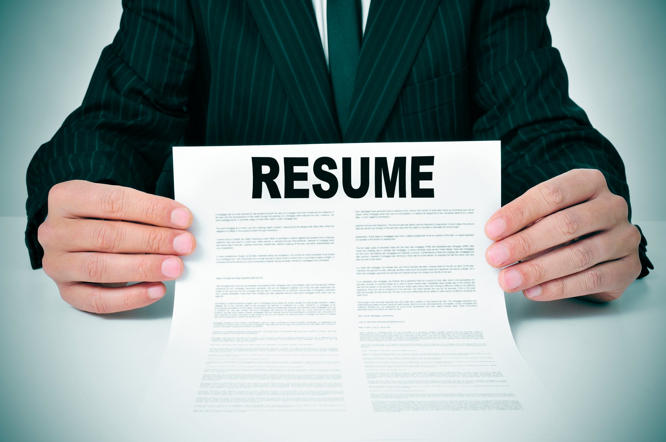 torso shown of man in suit holding a resume in front of him