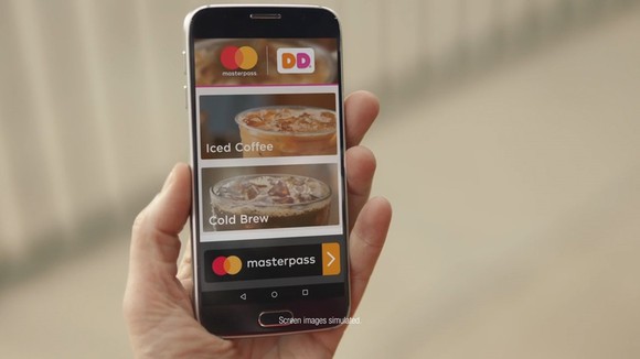 Hand holding mobile device displaying Mastercard's Masterpass and Dunkin' Donuts logos, along with mobile menu coffee images.