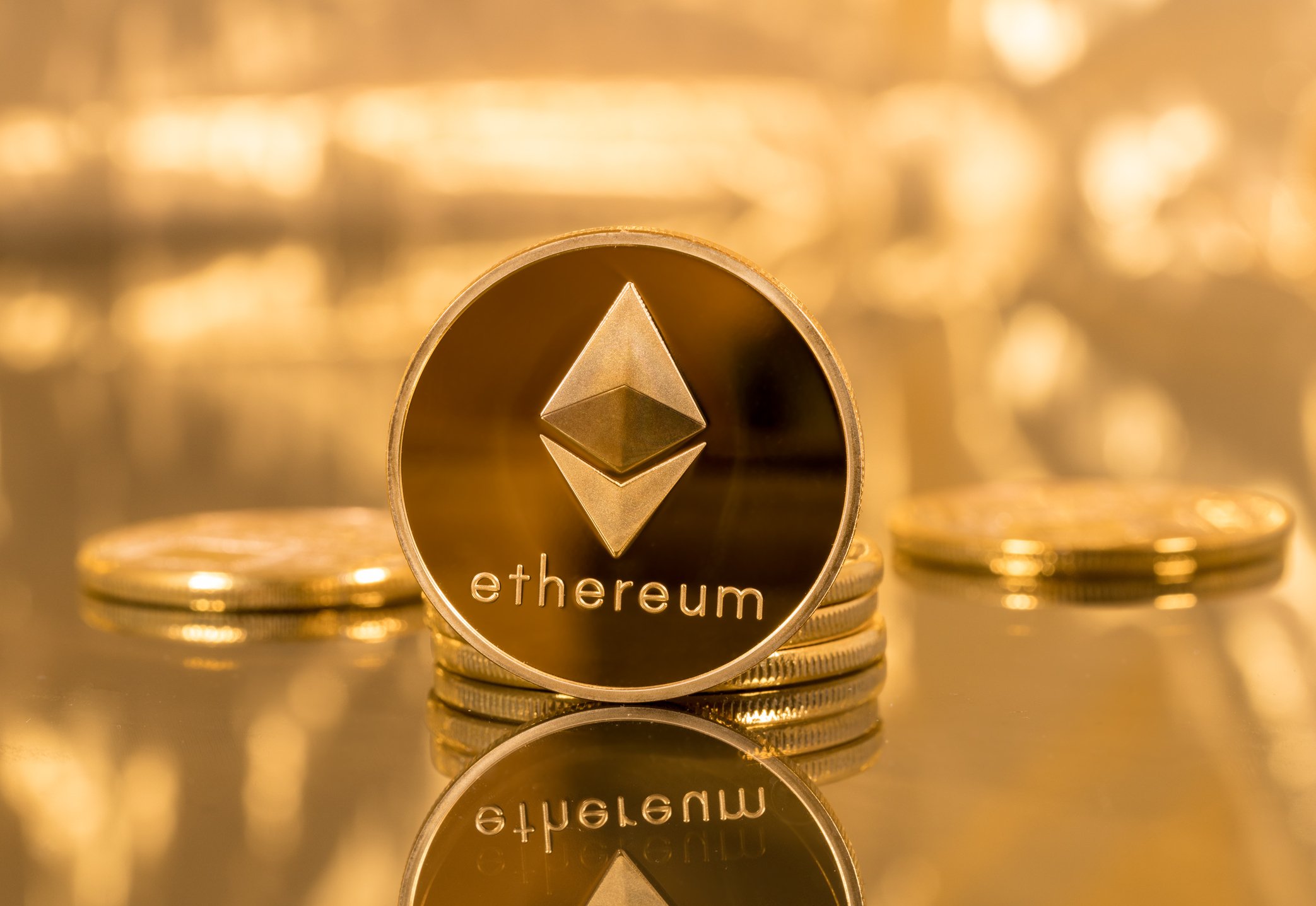 A gold-and-dark colored coin with "ethereum" on it, in front of a golden background.