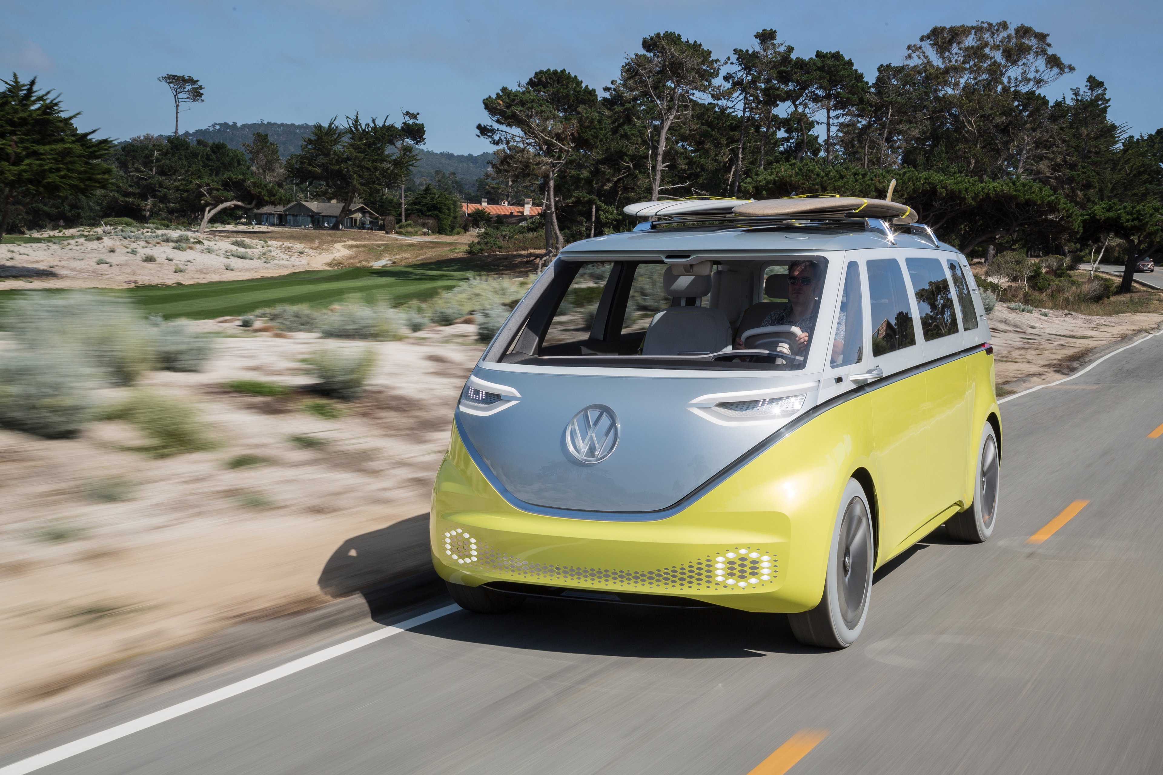 The VW I.D. Buzz, a yellow and silver electric minivan patterned after the historic VW Microbus, is shown cruising on a beach road in California. 