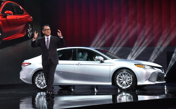 Toyoda is shown on an auto-show stage with a silver 2018 Camry sedan.