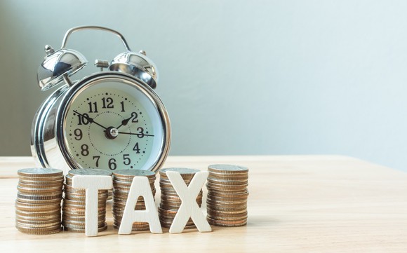 Old-style metal alarm clock with bells on top of a table, in front of piles of coins and TAX refrigerator magnets.