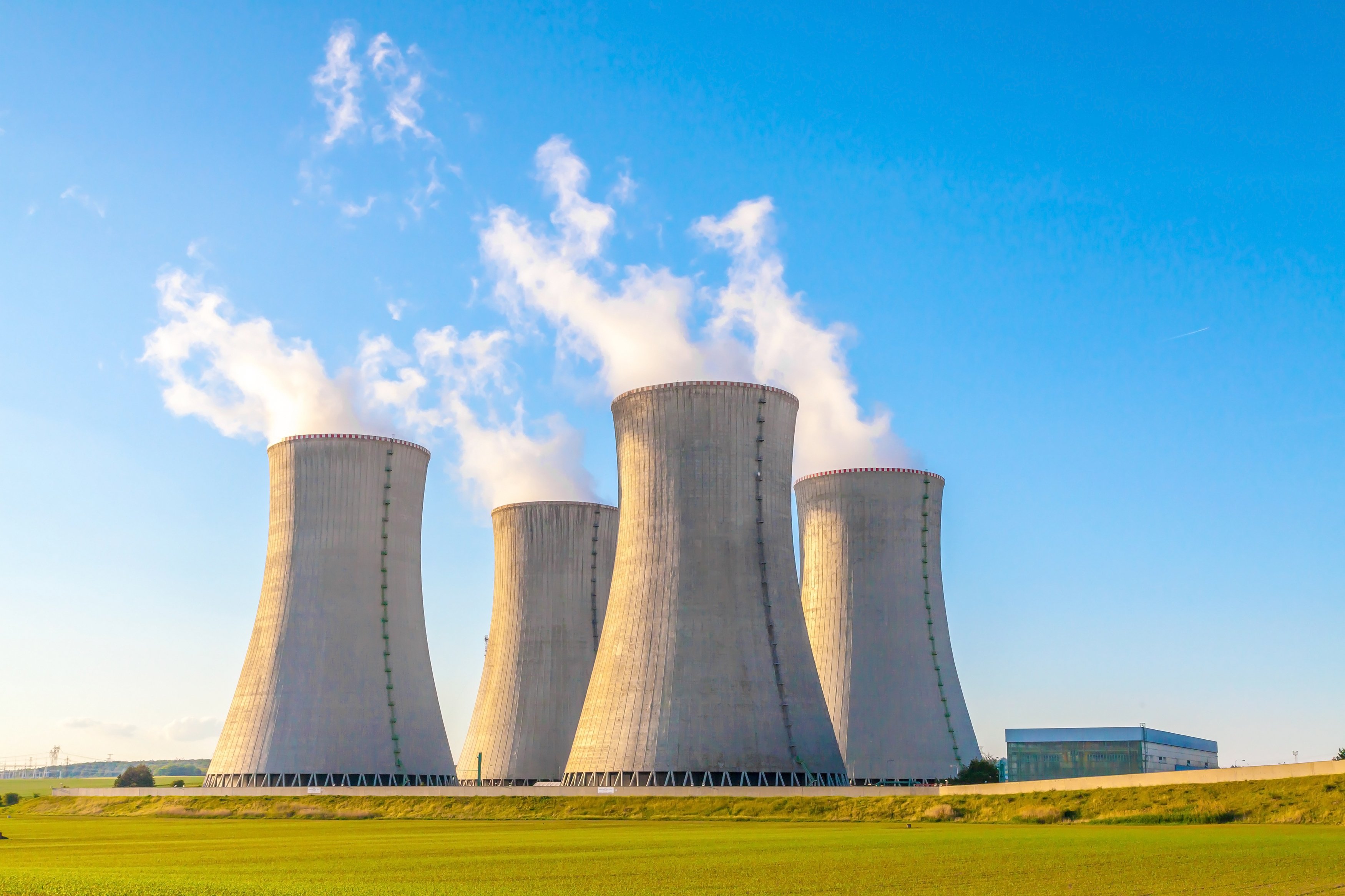 Four nuclear reactors with smoke billowing out of their stacks into a blue sky.