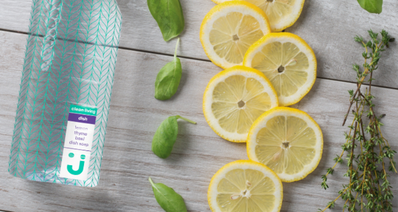 Uniquely J dish soap on wood table with sliced lemons and herbs.