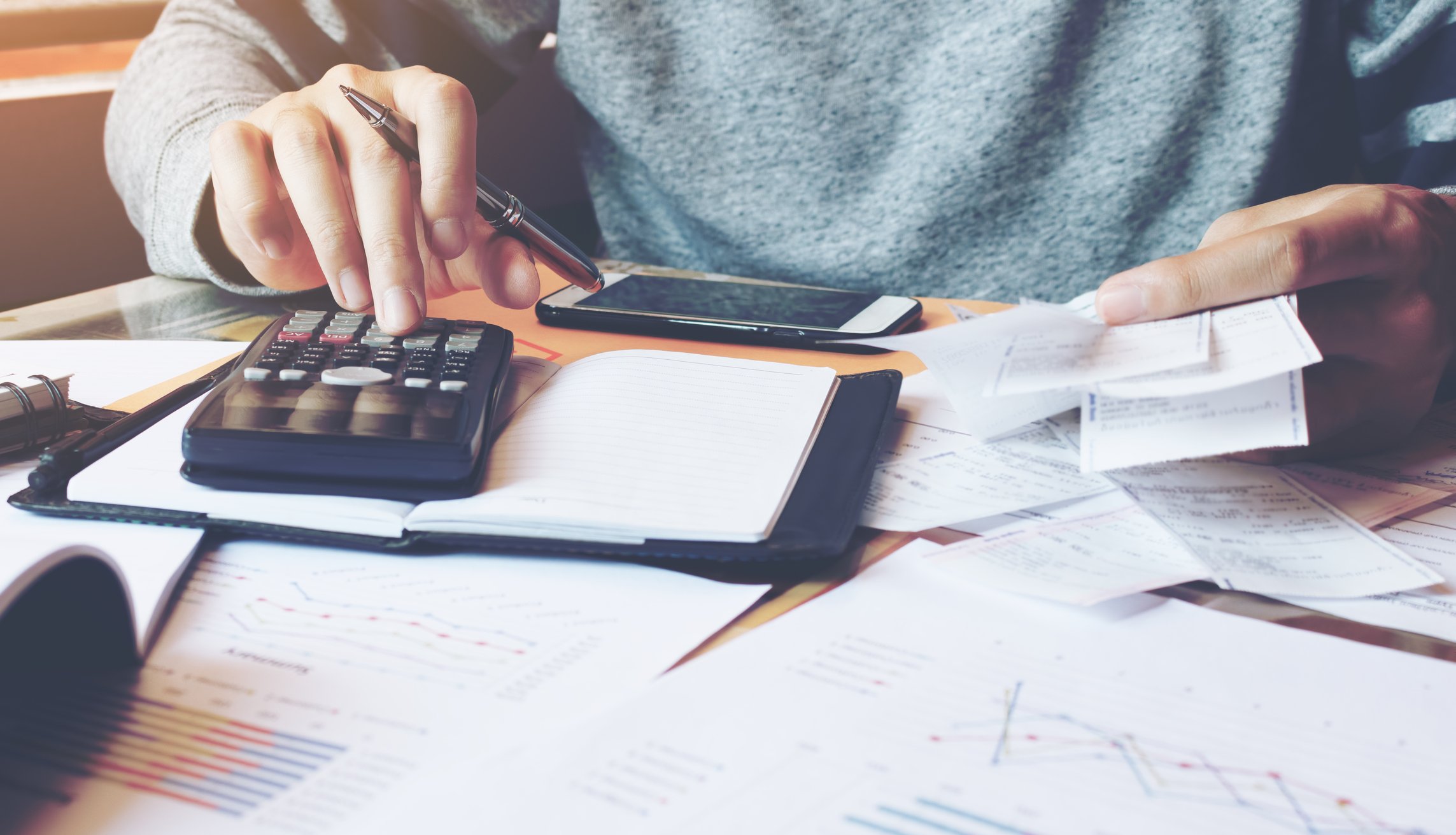 Person using a calculator with paperwork spread out on a desk