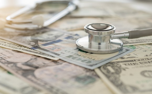A stethoscope sits on top of a scattered pile of U.S. currency.