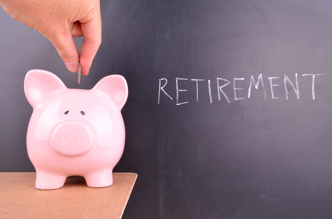 Hand placing change in a piggy bank next to the word "retirement" on a chalkboard.
