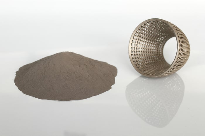 A pile of metal powder next to a 3D-printed metal part.