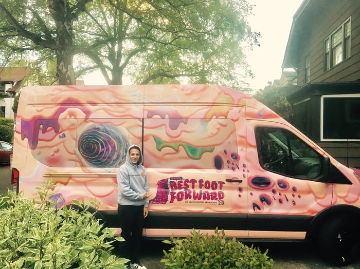 Pink-colored van labeled "Best Foot Forward" with person in hoodie in front of it.