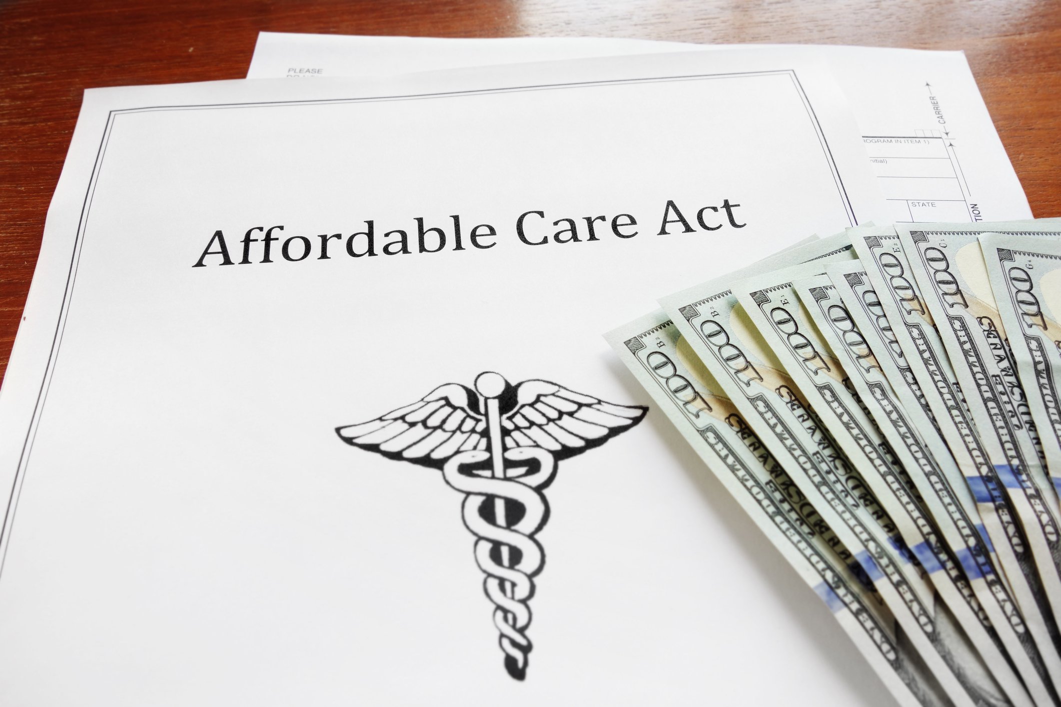Report labeled Affordable Care Act with medical symbol and $100 bills, on a wood desk.
