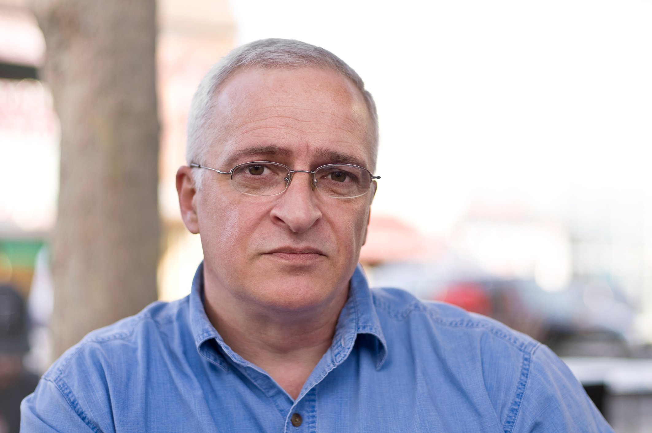 An older man seated outdoors with a serious expression.