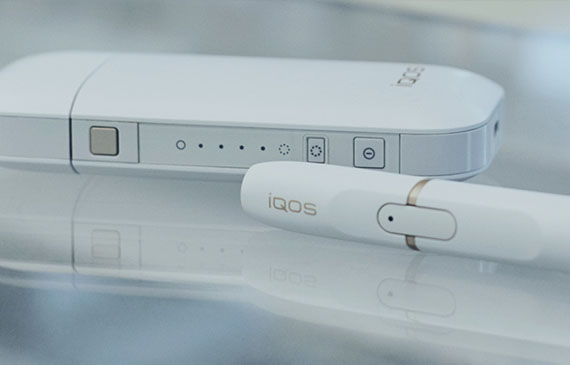 A closeup of IQOS, a white cartridge and white "cigarette" style delivery system.