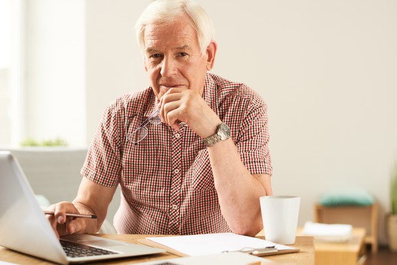 Senior male with a laptop, mug, and pad of paper