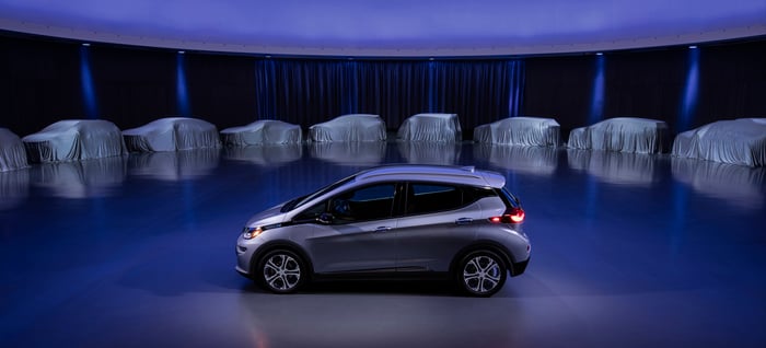 A Chevrolet Bolt EV is parked in front of a row of covered vehicles. 