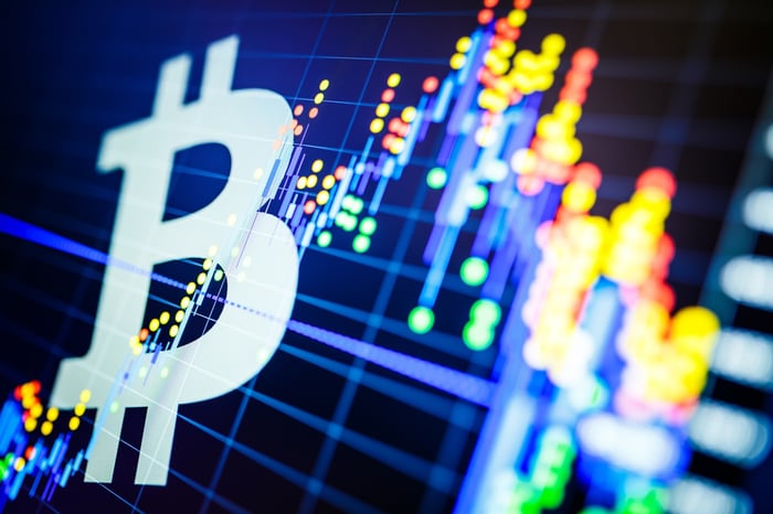 Bitcoin symbol in front of a candlestick price chart.