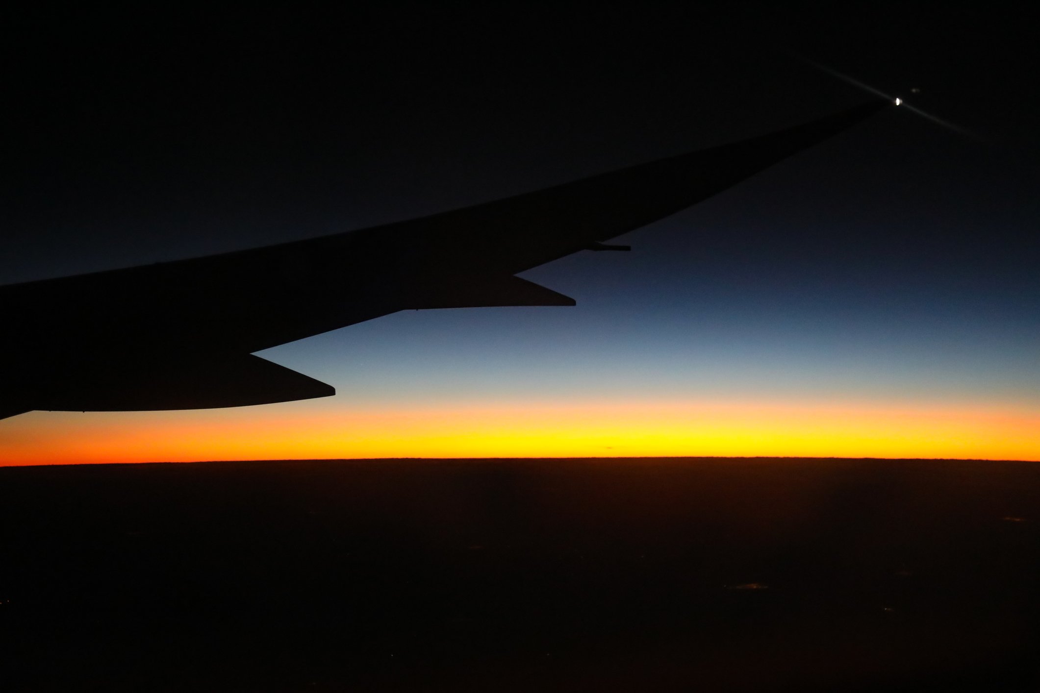 The wing of a Boeing Dreamliner in flight, silhouetted against the night sky.