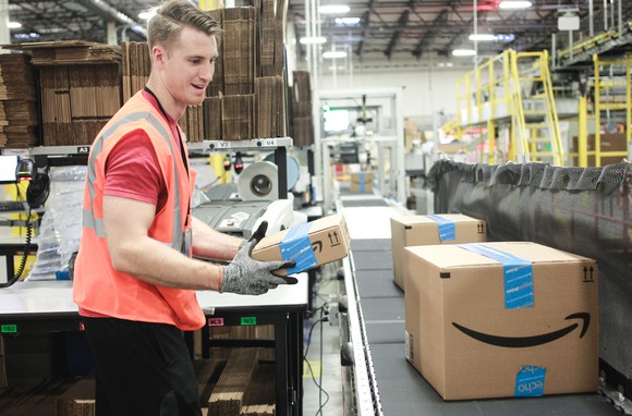 A warehouse worker placing an Amazon package on a conveyor belt.