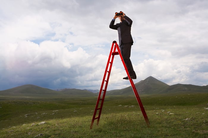 Man up a ladder looking into distance with binoculars.