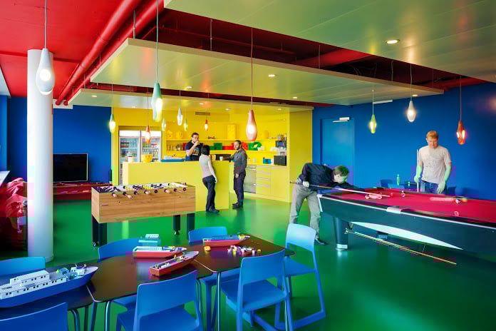 Workers relaxing in a brightly colored break room in Google's primary colors, featuring a pool table and some foosball action.