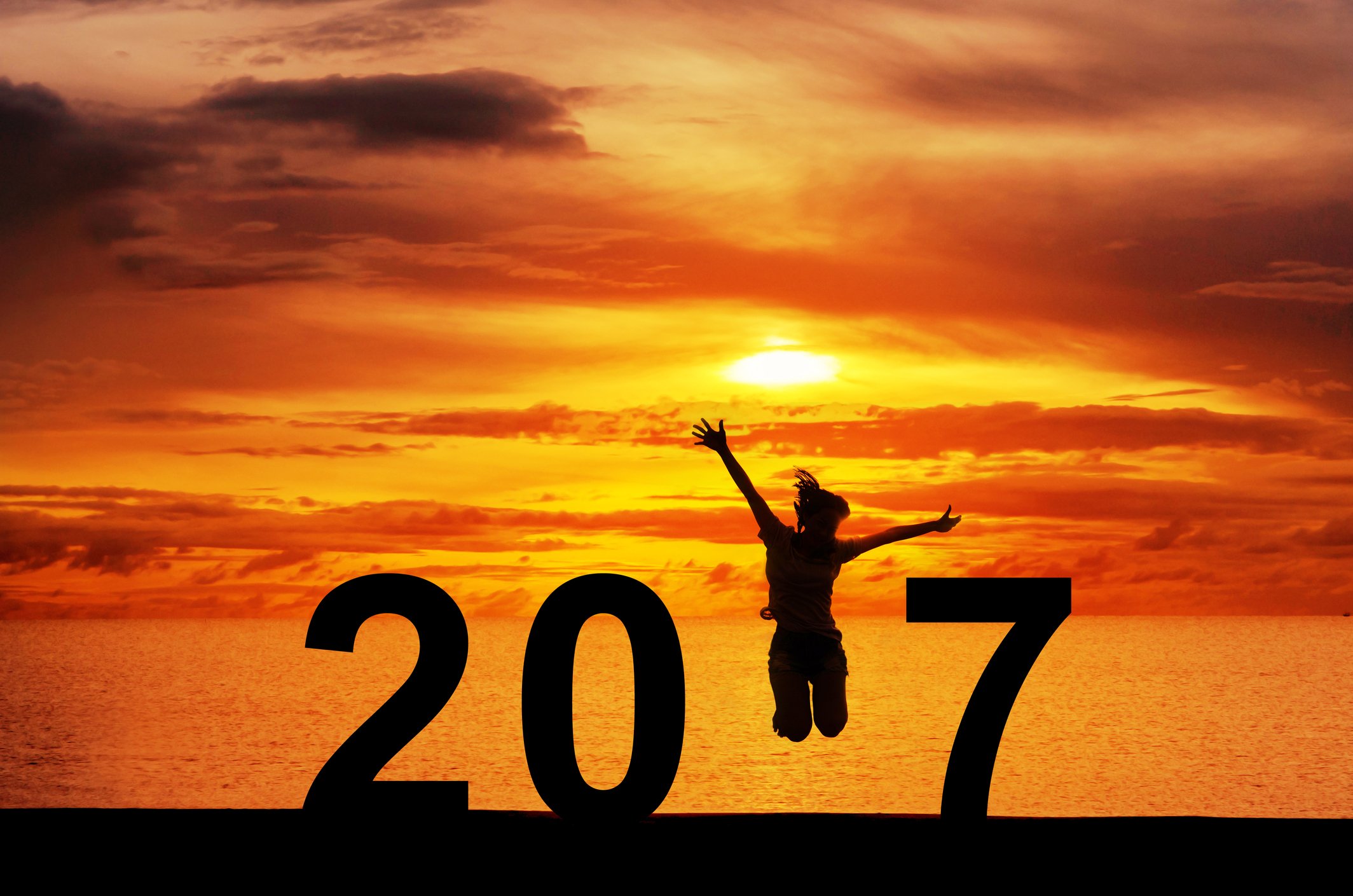 Silhouette of a woman jumping, as the "1" in "2017," with the ocean at sunset in the background