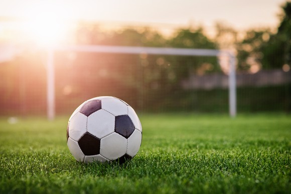 A soccer ball sitting on the grass in front of a goal.