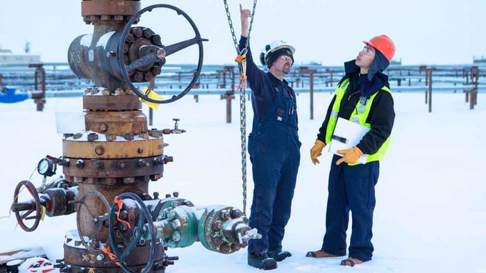 Two workers next to a wellhead having a conversation, on a field covered in ice or snow.