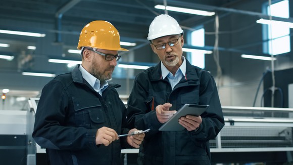 Men in hard hats looking at a tablet. 