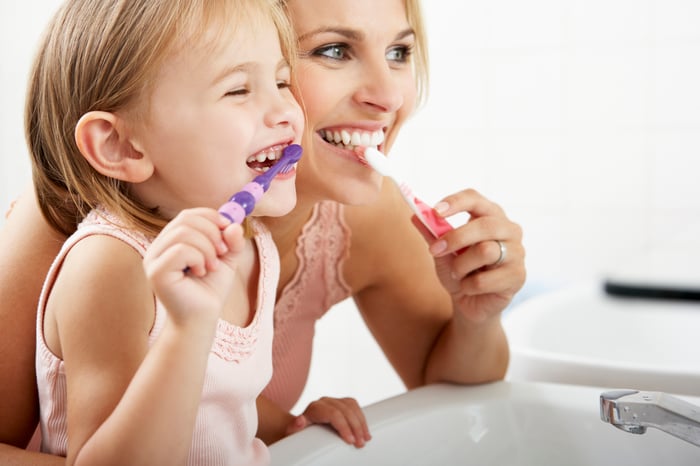 A mom and daughter brush their teeth together.