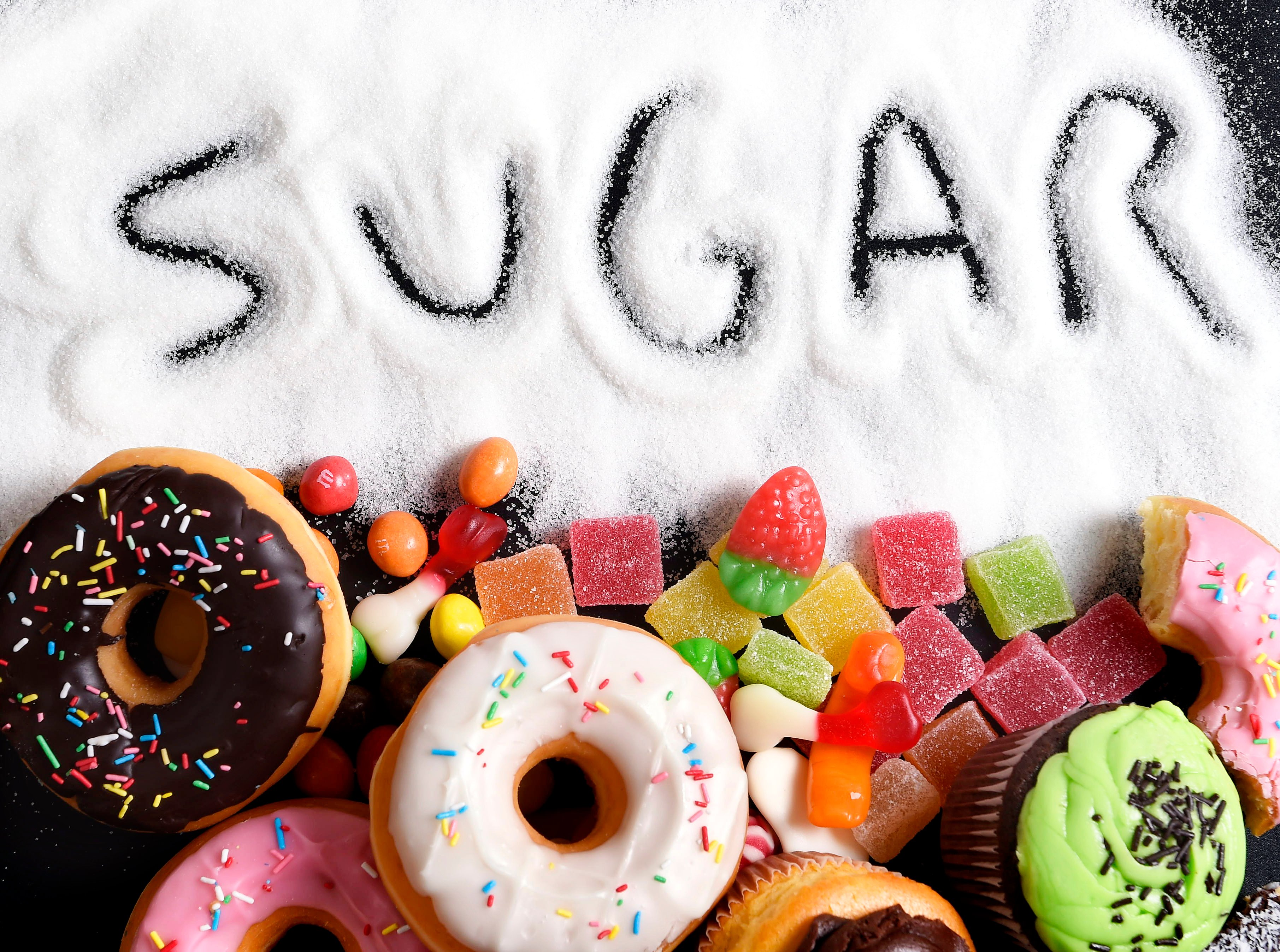 The word sugar drawn out in white sugar, next to donuts and candy. 