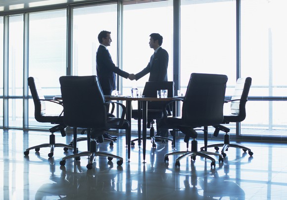 Two men shaking hands in a conference room.