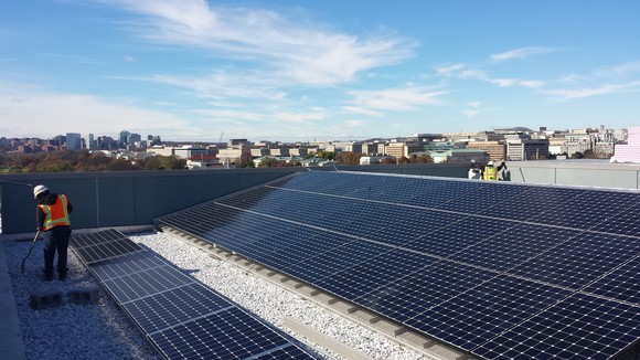 Solar panels on a large roof, with a worker shoveling gravel around the installation site. 