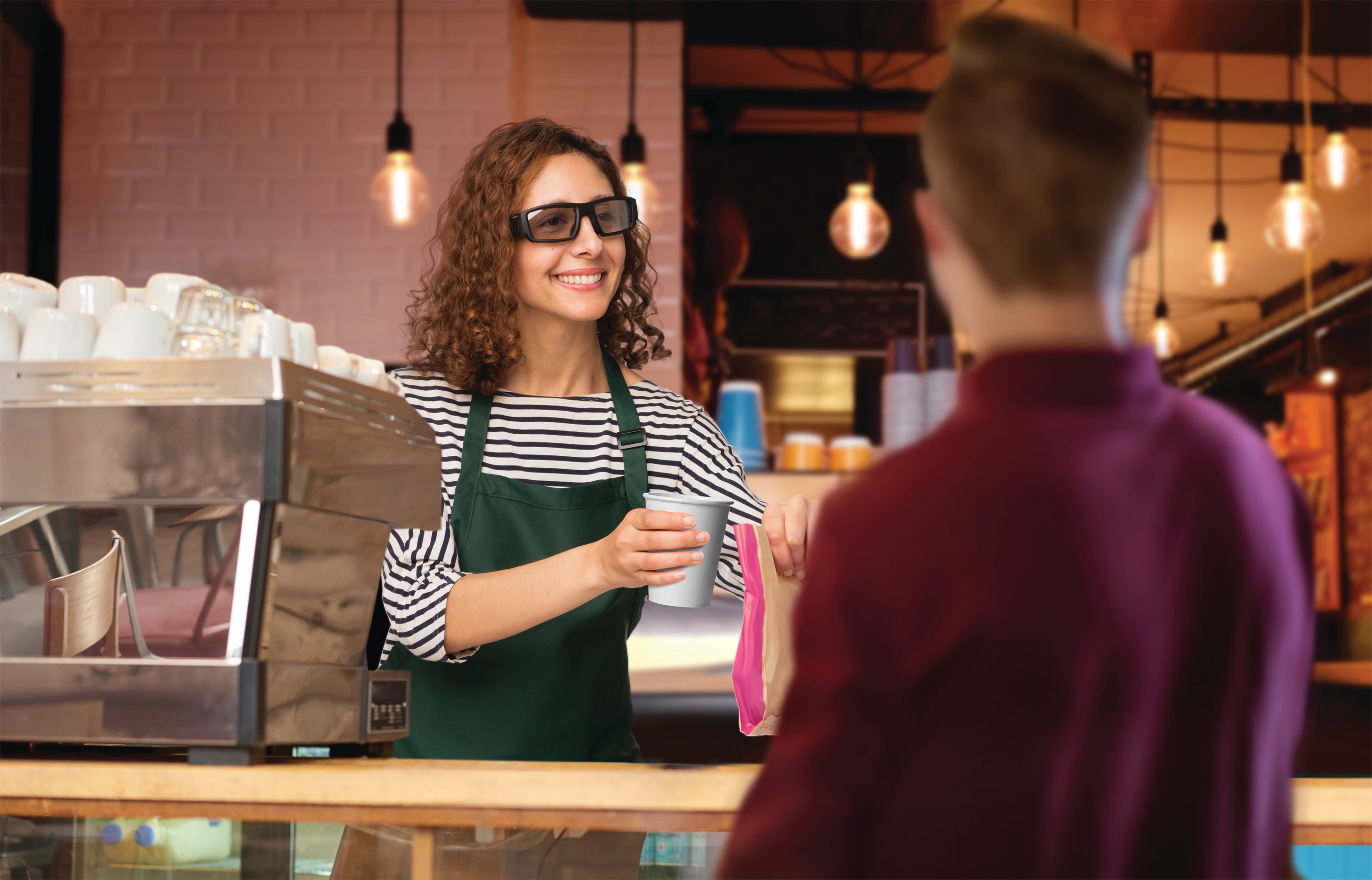 A barista wearing Vuzix Blade 3000 smart glasses serving coffee to a customer