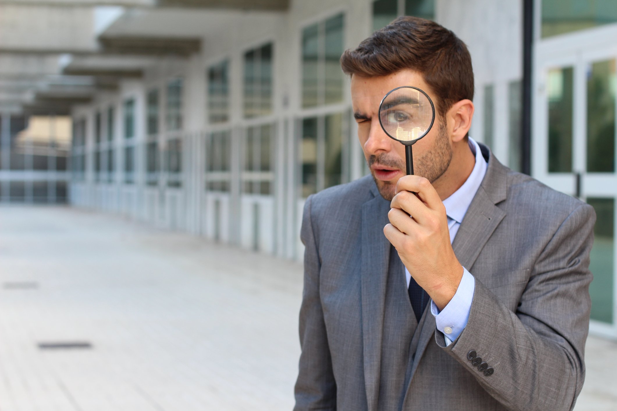 Man in a suit on the sidewalk looking through a magnifying lens.