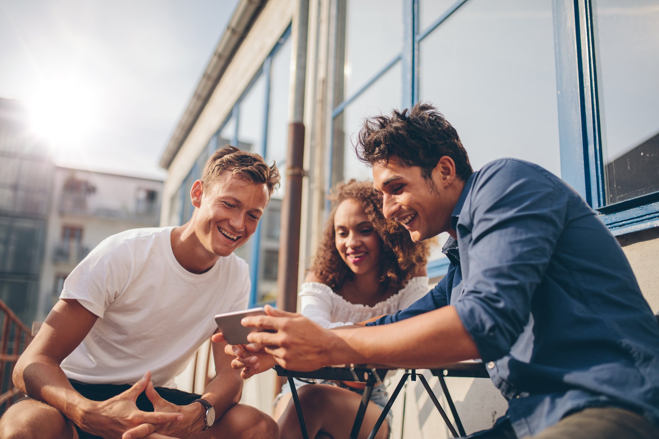 Two young men ad a young woman watch a video on one their smartphones. 