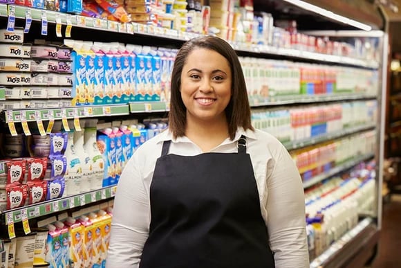 A Kroger employee stands in front of a cooler full of grocery items.