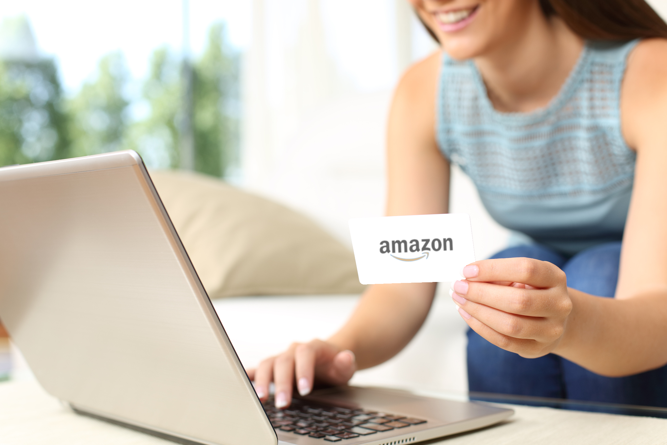 Smiling woman using a laptop while holding a credit card that features Amazon's corporate logo.