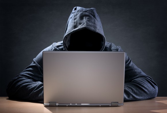 A hooded individual using a laptop.