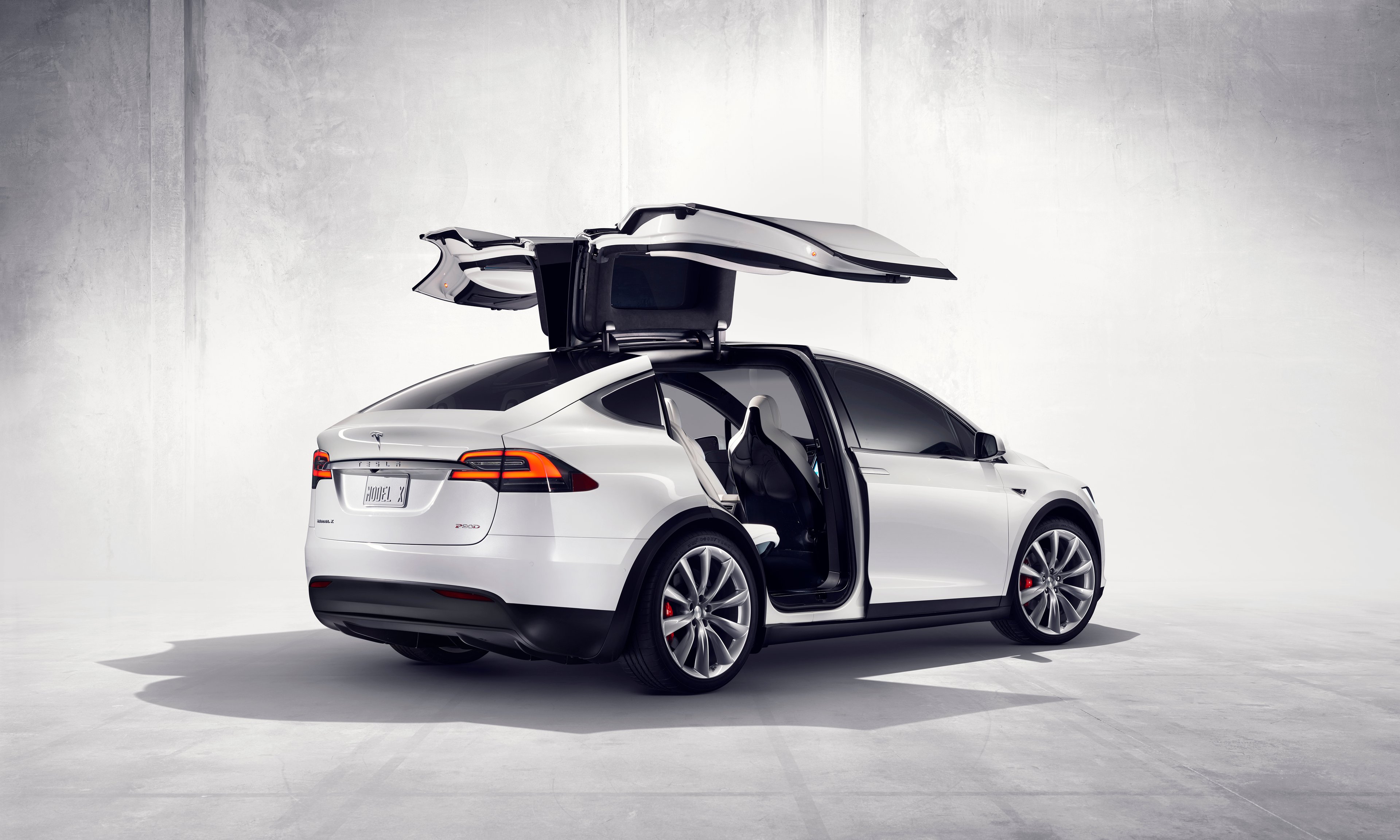 A white Tesla Model X with its gull-wing doors open