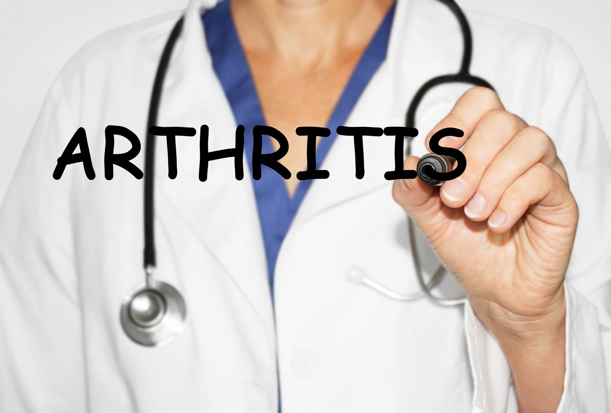 A doctor writes the word arthritis on a transparent surface.