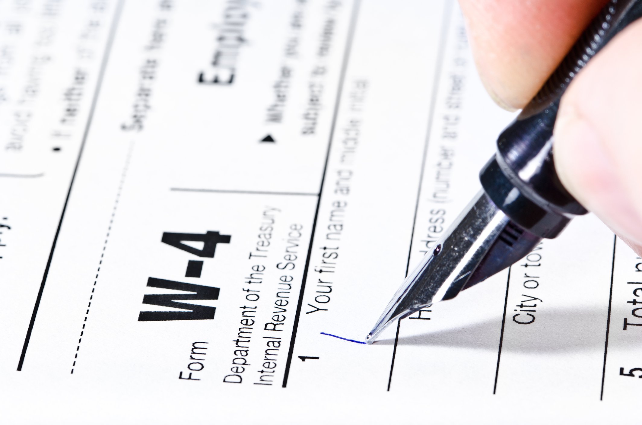 A hand holds a pen and begins filling out Form W-4
