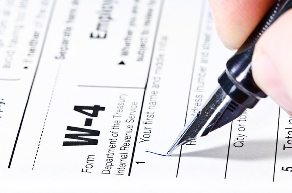 A hand holds a pen and begins filling out Form W-4