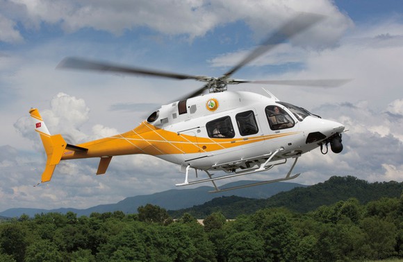 Yellow and white Textron Bell 429 Helicopter flying with mountains in the background