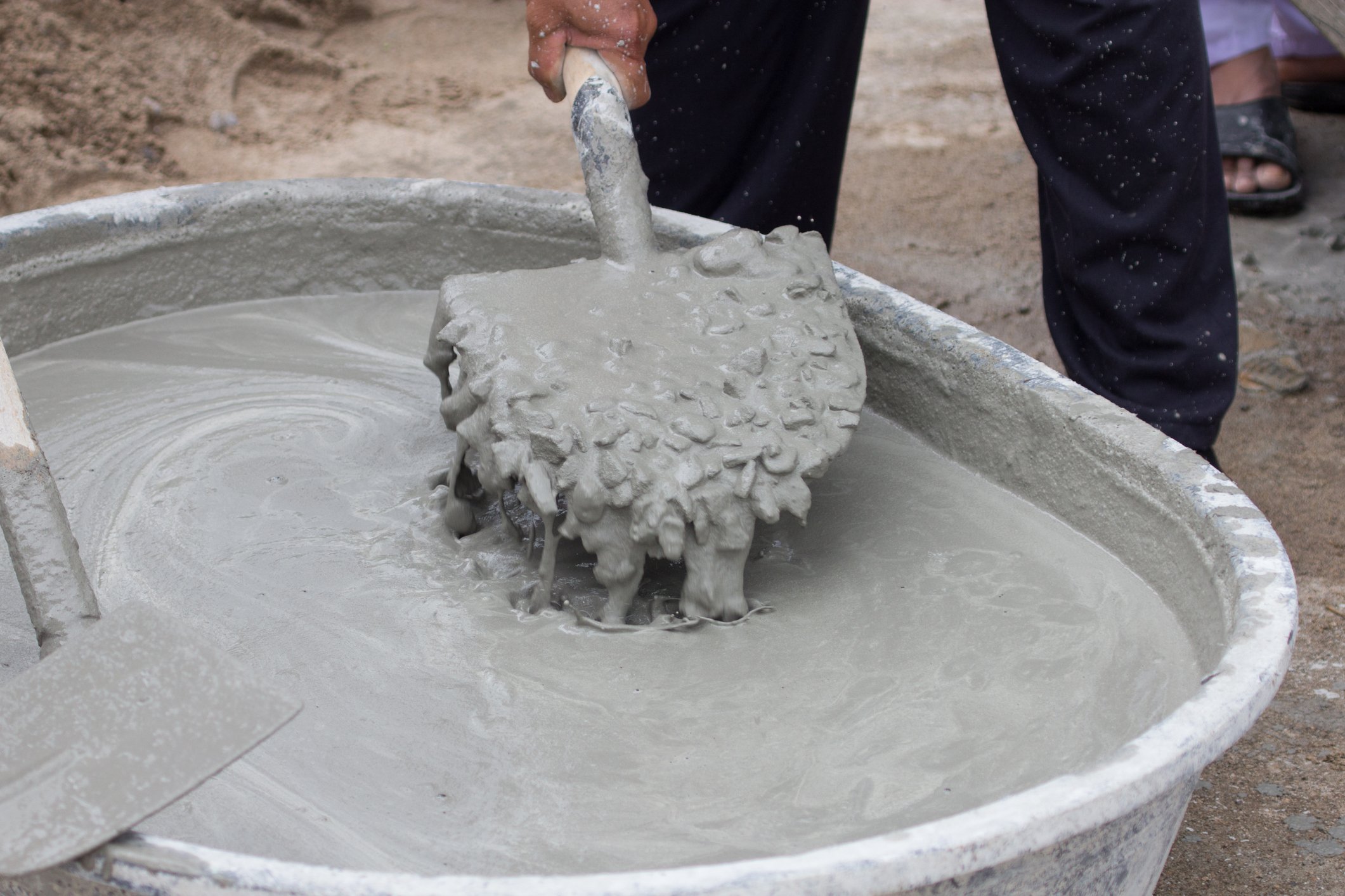 A person mixing cement with a shovel.