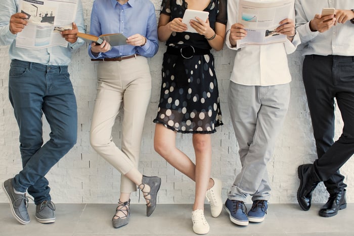 People look at a variety of print products and digital devices while standing in a row.