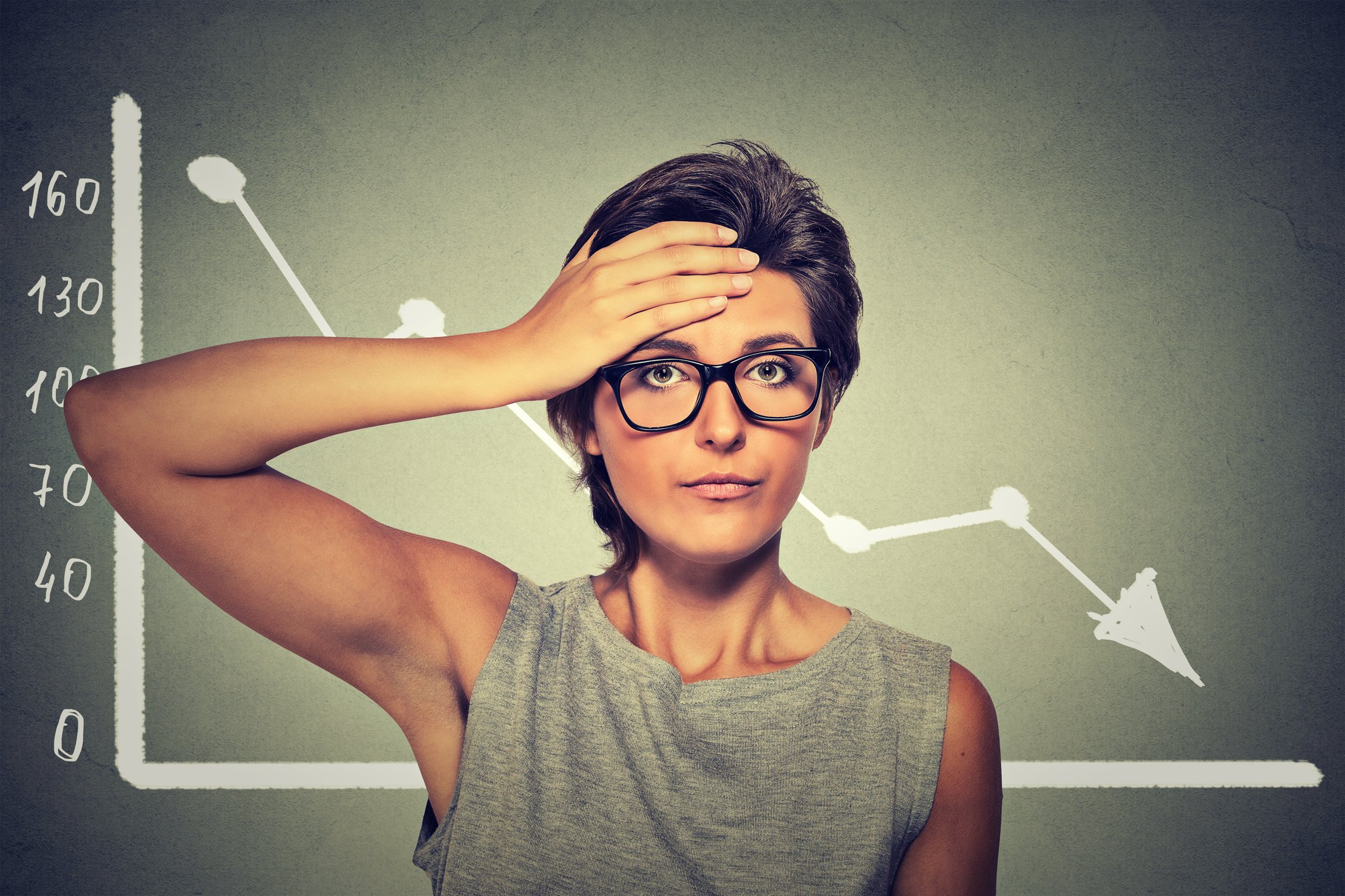 A chart showing a downward trend with a person with hand on their forehead standing in front of it.