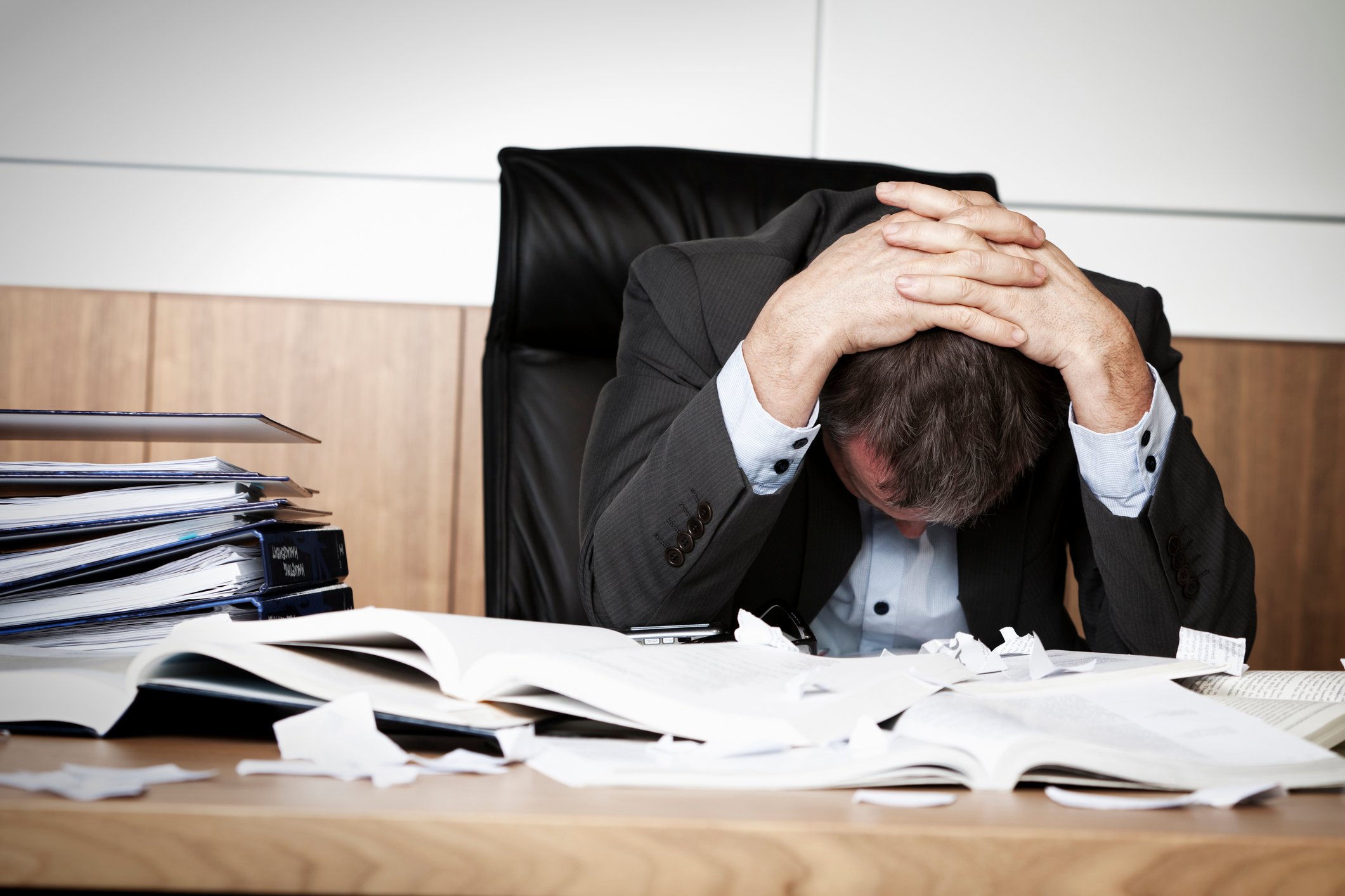 Man holding his head, looking at a desk full of papers