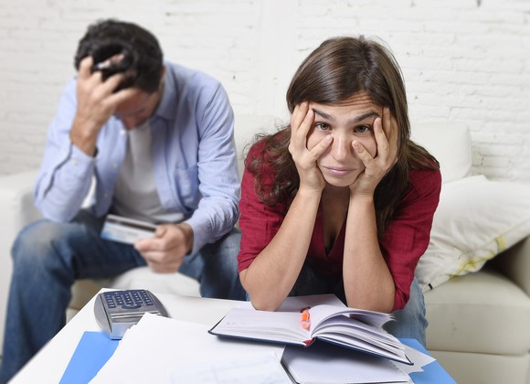 a young couple looking upset, with heads in hands, with calculator and papers