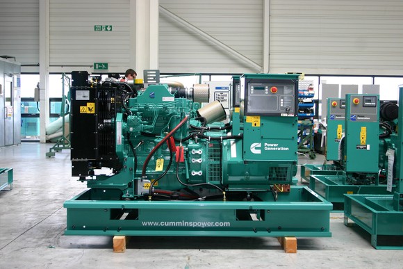 Green-colored power generation equipment in a factory setting, with a worker behind the unit.