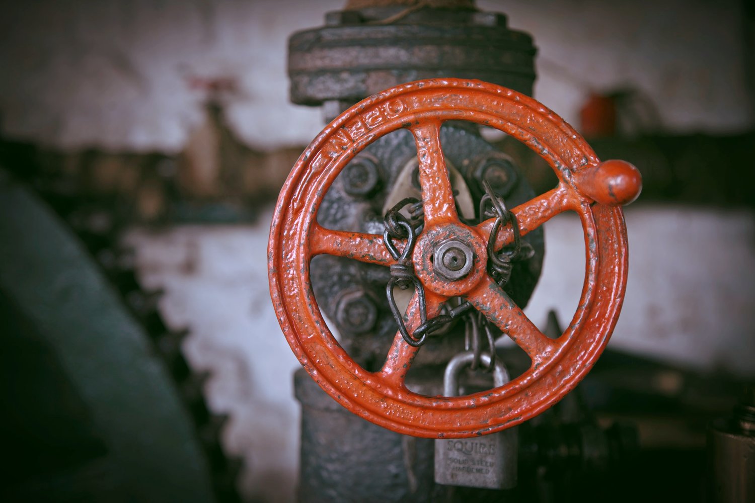 Red circular valve attached to a gray-brown pipe.