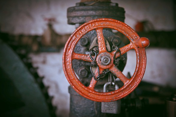 Red circular valve attached to a gray-brown pipe.